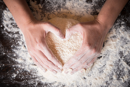 Female hands holding dough in heart shape