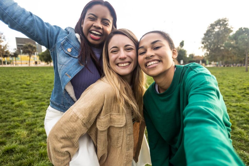Three young college-aged women huddled together and smiling on campus wearing casual clothes.